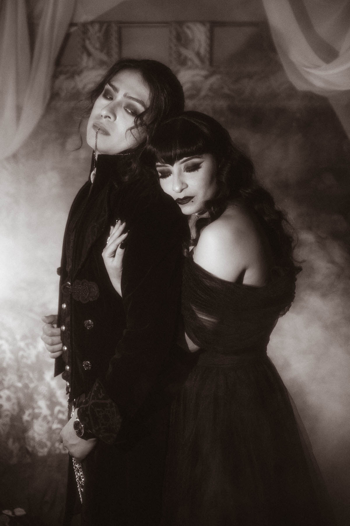 Black and white portrait of a couple embracing in fog beside sheer drapes for gothic engagement photography in Dallas