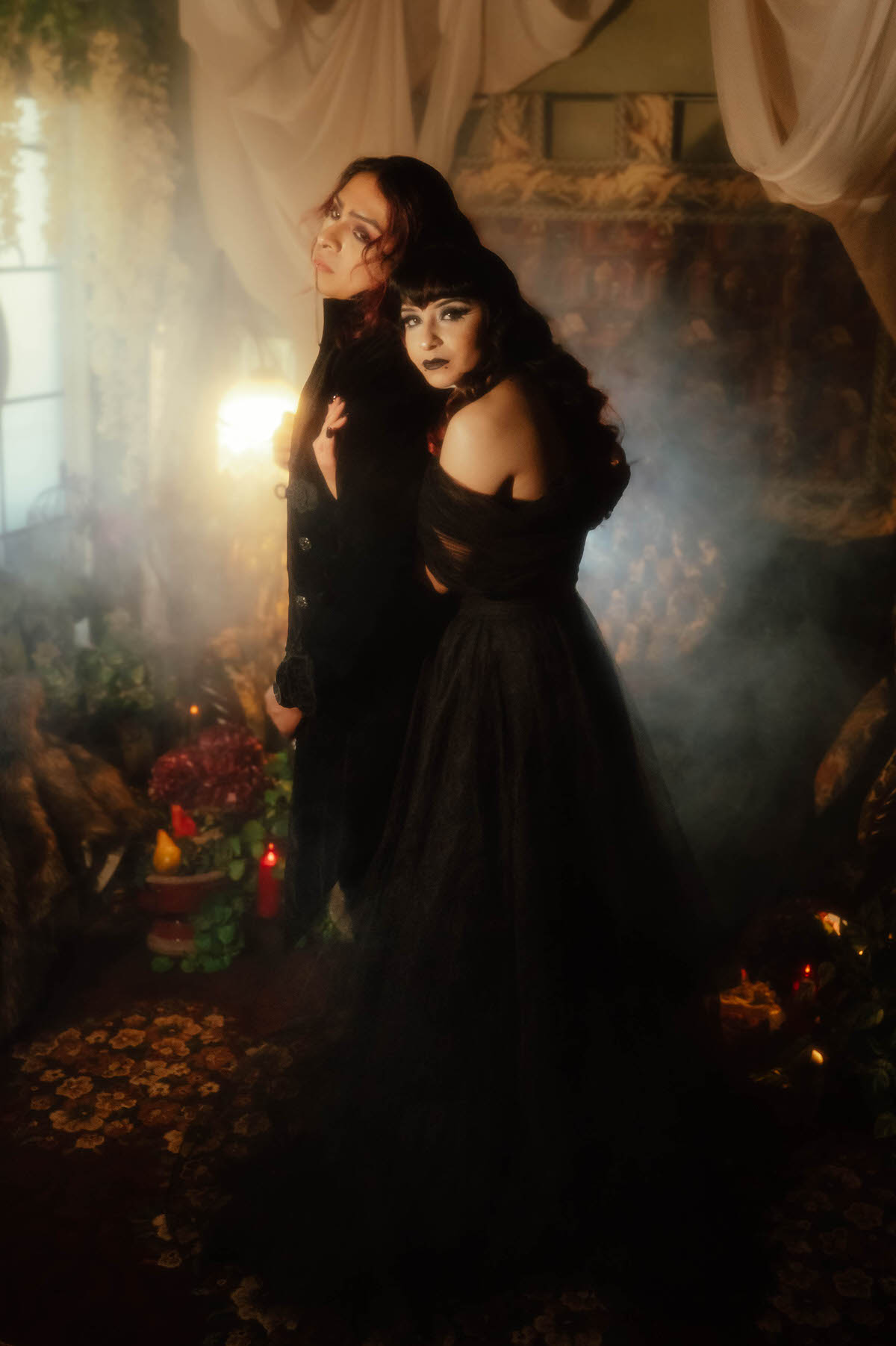 Couple in a black gown and black suit posed in fog near red candles for a mood engagement session in Dallas