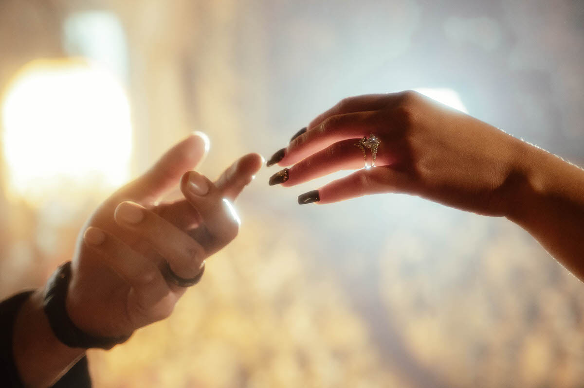 Hands with rings reaching toward each other in warm backlight for dark fantasy engagement photos