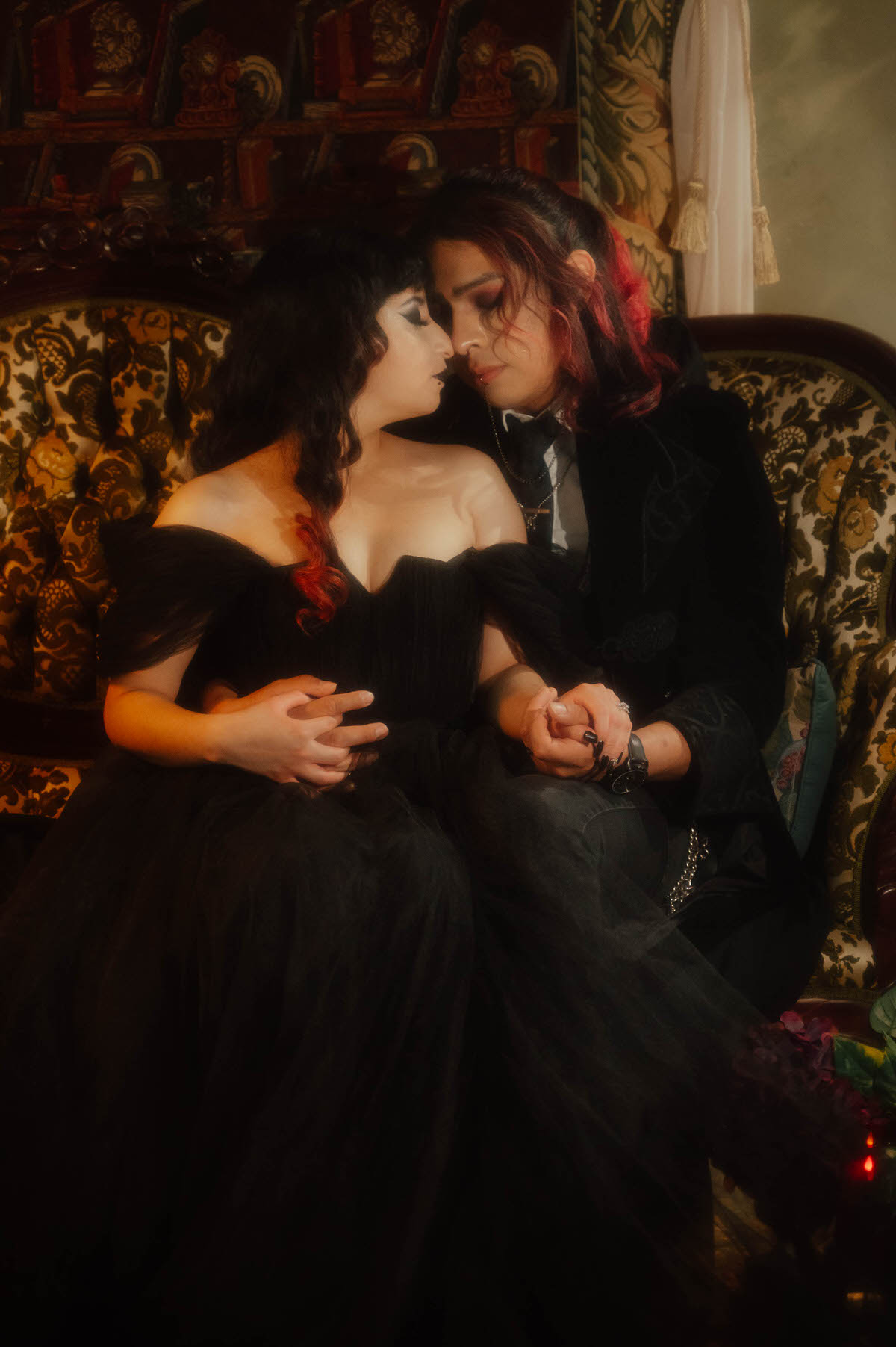 Couple sitting close with foreheads touching on a floral tufted sofa for gothic bride and groom photos