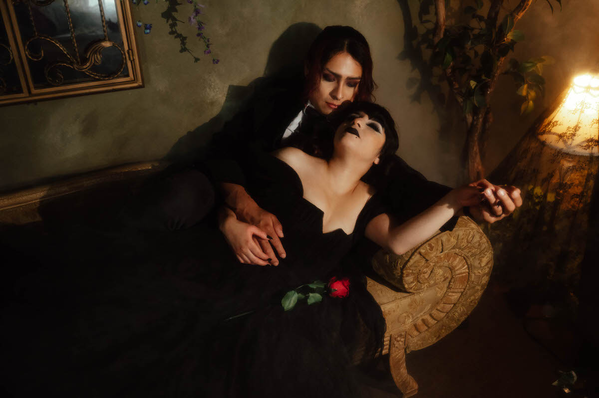 Couple reclining on a chaise with a red rose and a glowing lamp for gothic engagement photography in Dallas