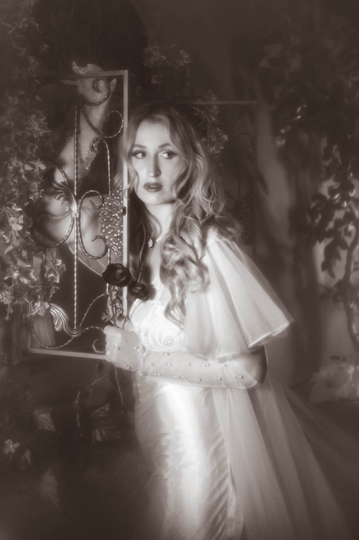A black and white boudoir portrait shows a woman in a vintage ivory satin slip and sheer chiffon robe standing beside a gilded frame with a dark rose in her pearl beaded glove, adding a moody vintage boudoir photography DFW feel to this dreamy boudoir photoshoot with Royal Lune Photo.